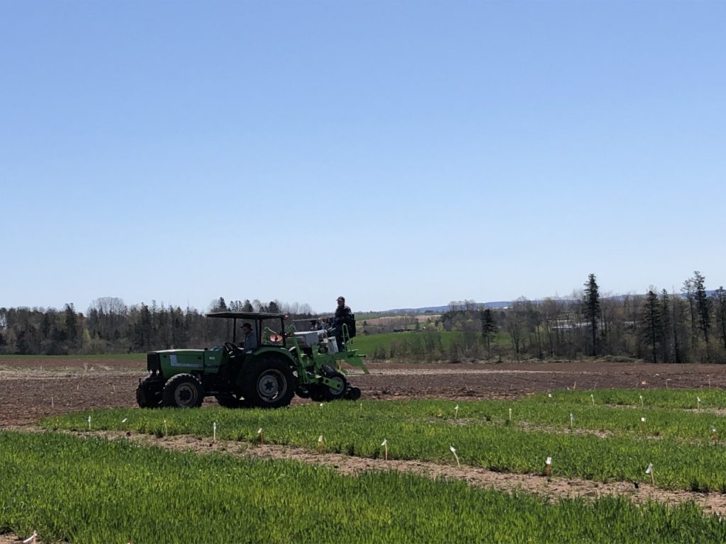 A tractor on a field with two people operating the equipment on a sunny June day.